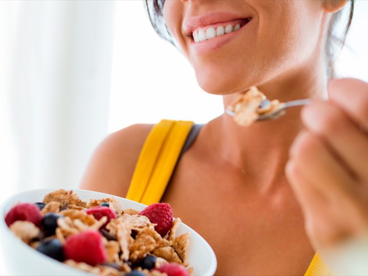 Mulher sorrindo enquanto come uma tigela de granola com frutas vermelhas
