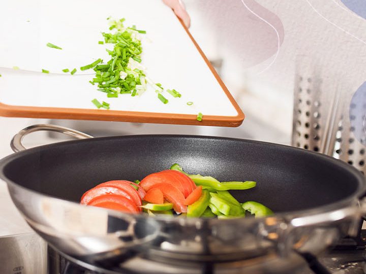 Legumes frescos sendo refogados na panela, com cebolinha picada na tábua