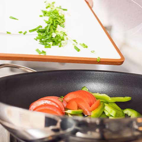 Legumes frescos sendo refogados na panela, com cebolinha picada na tábua